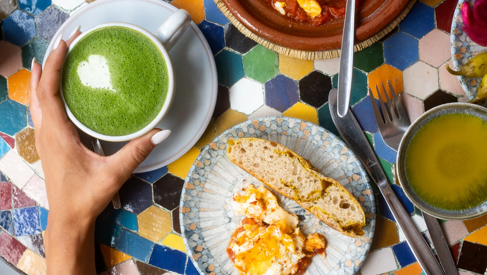 Frühstückstisch mit Matcha Latte, Brot, Rührei und Suppe auf einem bunten Mosaiktisch