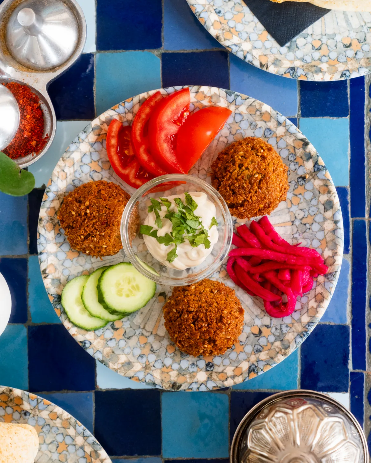Teller mit Falafel, Hummus, Tomaten, Gurken und eingelegter Mairübe auf einem Mosaiktisch