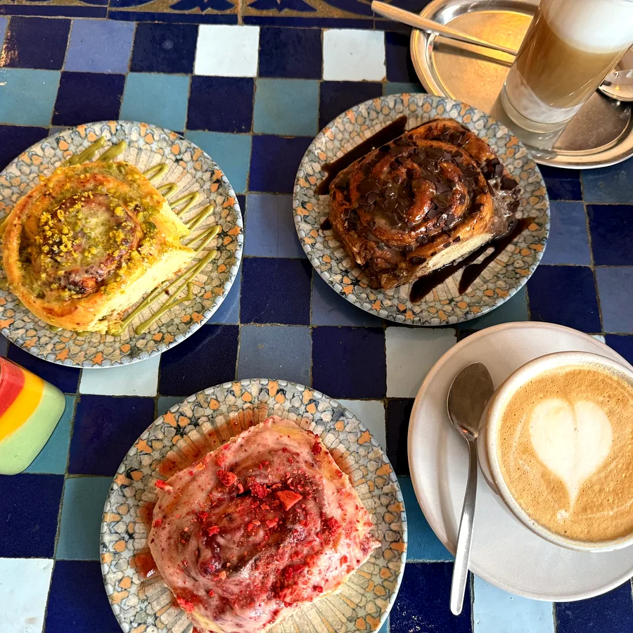 Drei Gebäckstücke und ein Cappuccino auf einem Mosaiktisch