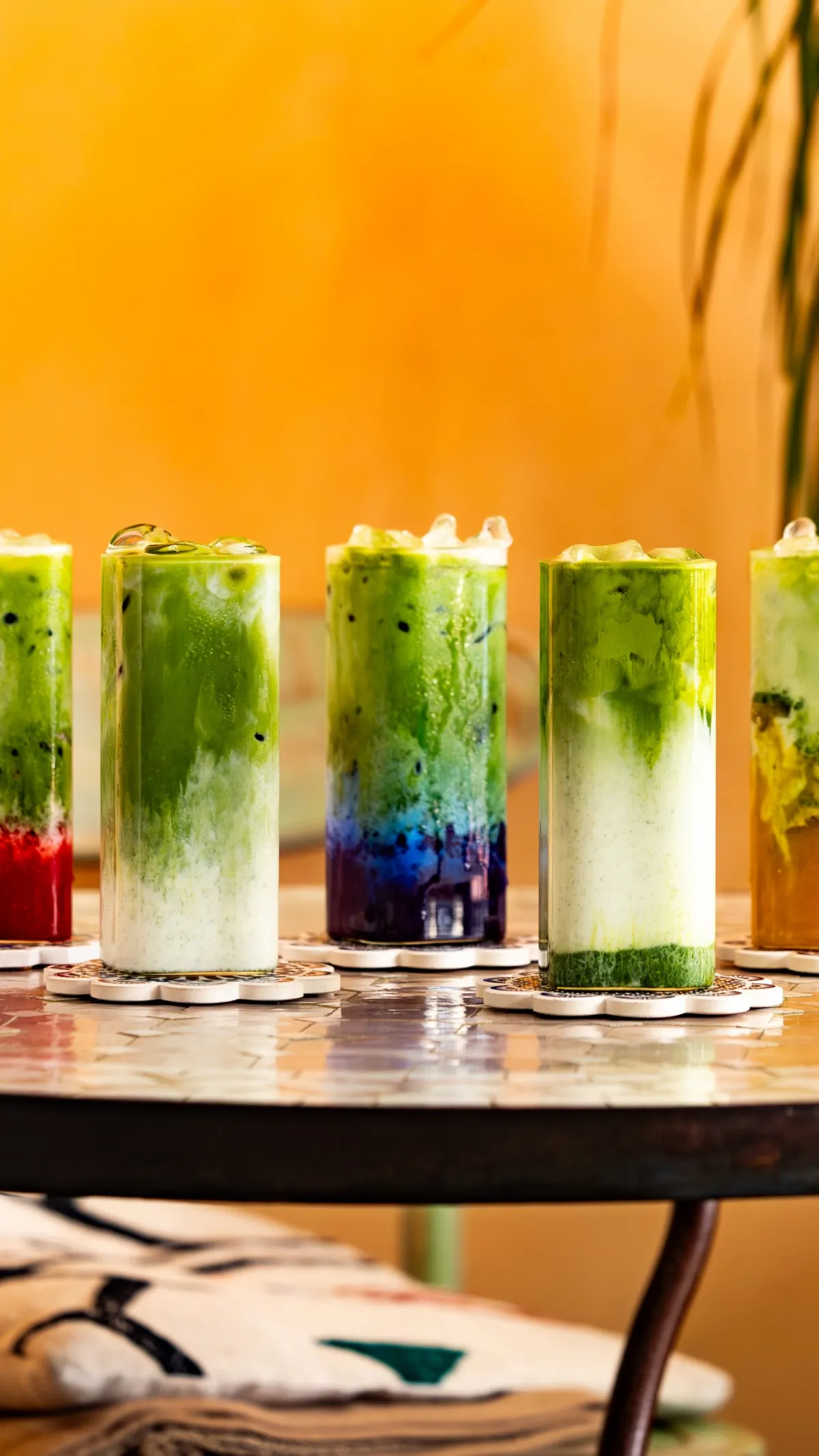 Reihe von Iced-Matcha-Gläsern vor einer orangefarbenen Wand