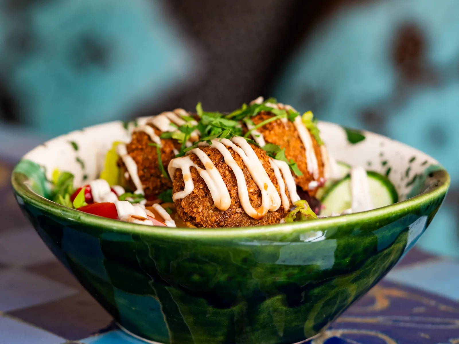Falafel-Bowl mit Sesamsauce in einer grünen Schale vor türkisfarbenem Hintergrund