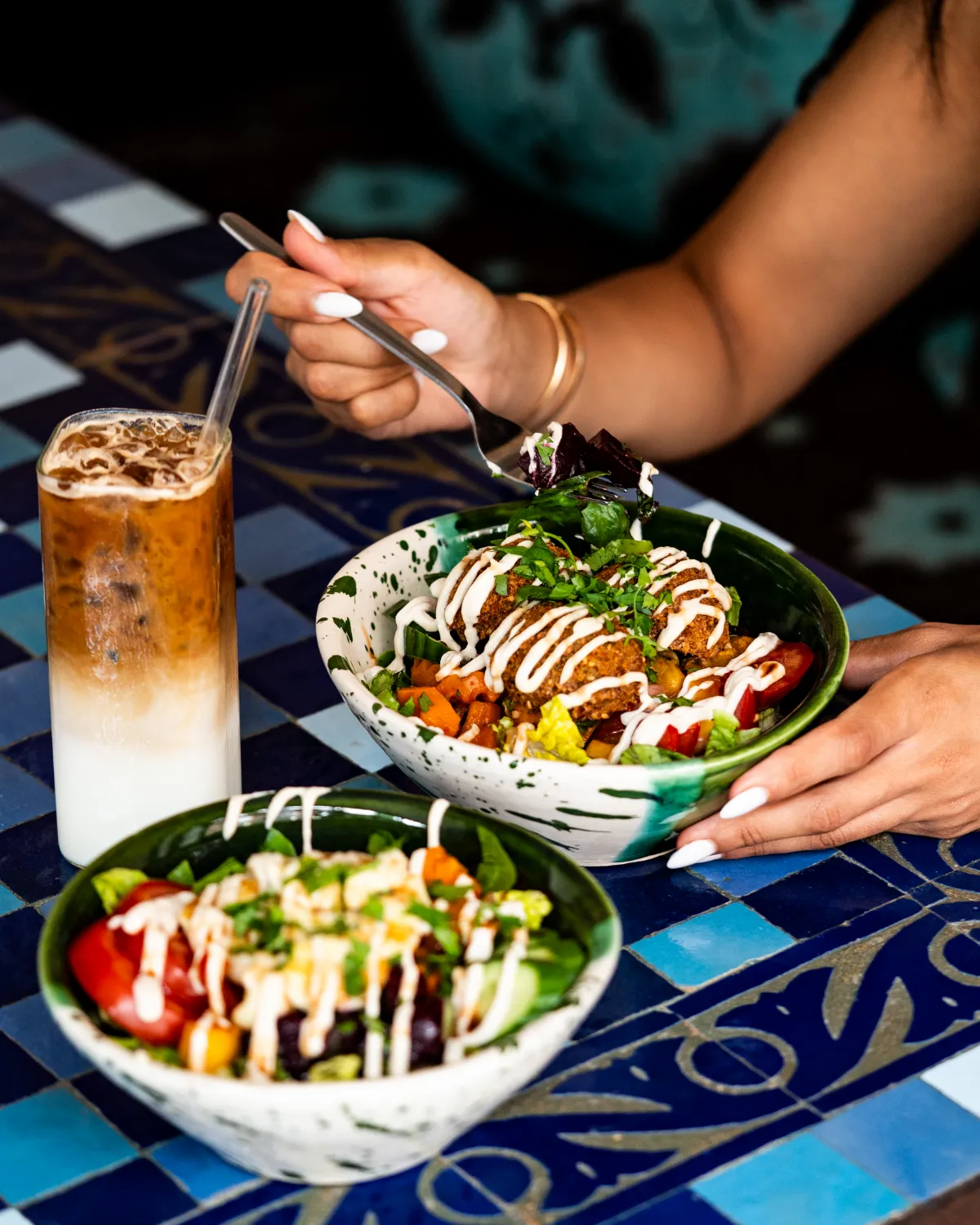 Salatbowls mit Falafel und ein Iced Latte auf einem blauen Mosaiktisch